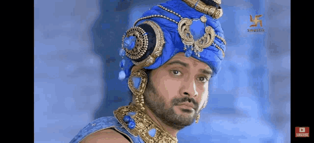 a man with a beard wearing a blue turban and gold jewelry .