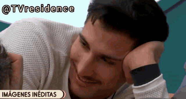 a man with his head resting on his hand is smiling in front of a sign that says " imagenes ineditas "