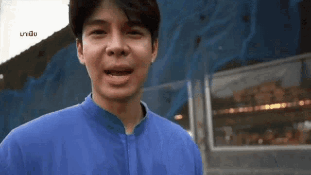 a man in a blue jacket is making a funny face while standing in front of a fence .