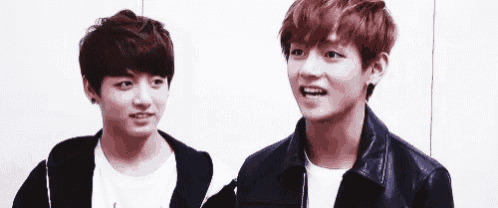 two young men are standing next to each other and looking at each other . one of the men is wearing a leather jacket .