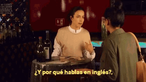 a woman sitting at a table talking to another woman with the words y por que hablas en ingles on the bottom