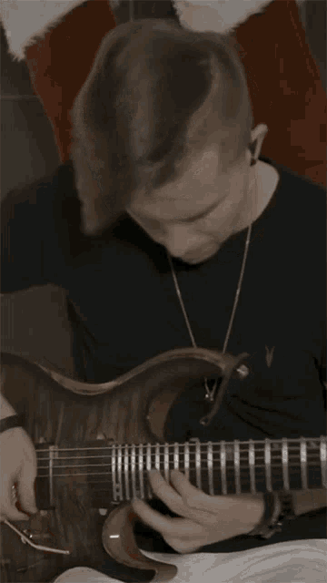 a man in a black shirt is playing a guitar with the letter v on the neck