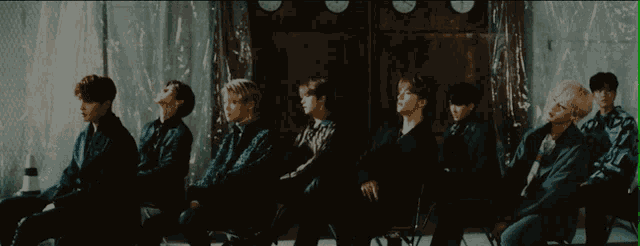 a group of young men are sitting in chairs in front of a wall with clocks on it