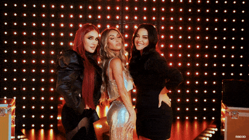 three women pose in front of a wall of lights with hbo3d written on the bottom left