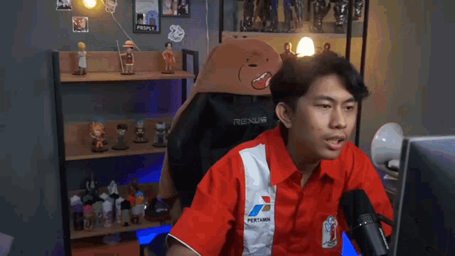 a man in a red rexus shirt sits in front of a computer monitor