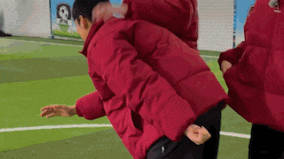 a man in a red jacket is carrying another man on his back on a soccer field .
