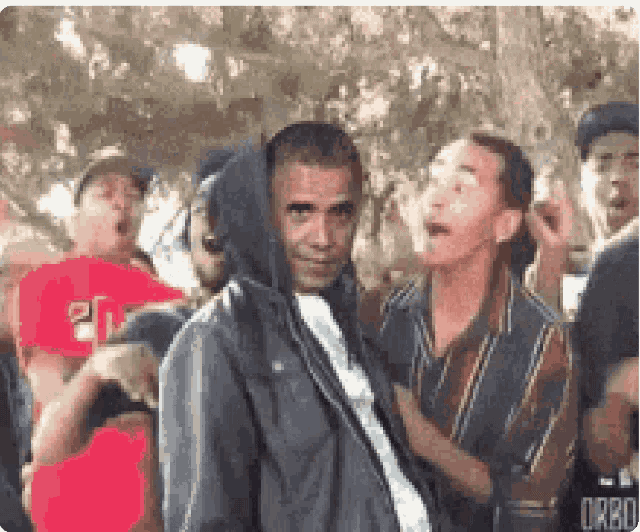 a man wearing a hooded jacket is surrounded by other people .