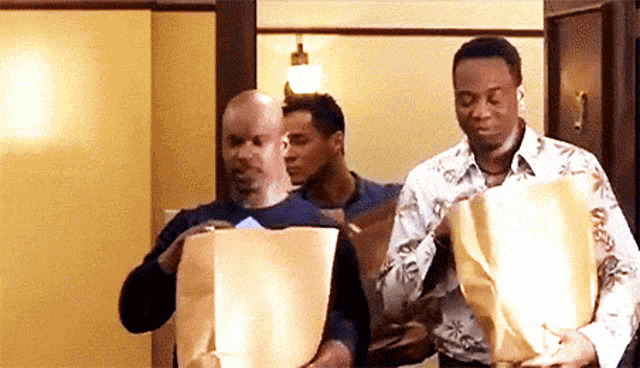 three men are standing in a room carrying bags of paper .