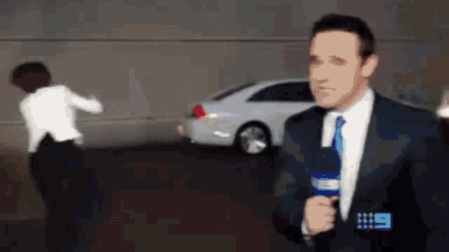 a man in a suit and tie is holding a microphone while a woman stands in the background .