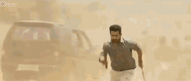 a man with a beard is holding a sword and running in the sand .