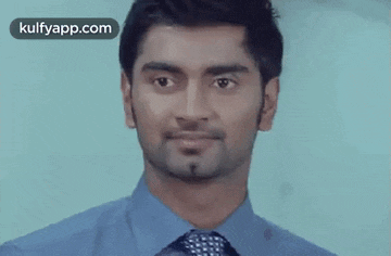 a man in a blue shirt and tie looks at the camera