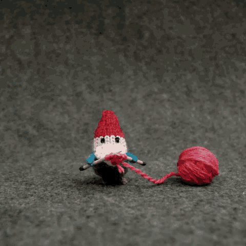 a knitted gnome with a red hat is holding a ball of yarn