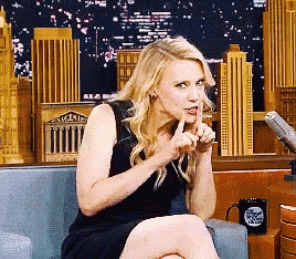 a woman in a black dress is sitting on a couch with her finger to her lips
