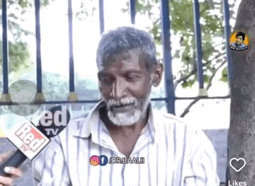a man with a beard is talking into a microphone while sitting under a tree .