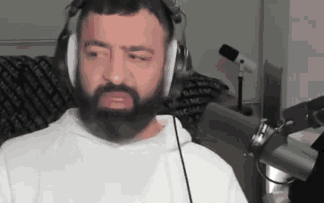 a man with a beard is wearing headphones and a headset while talking into a microphone .