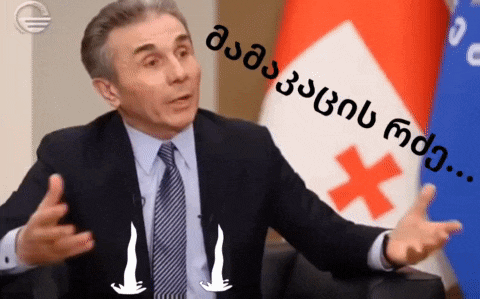 a man in a suit and tie is talking in front of a flag that has a cross on it