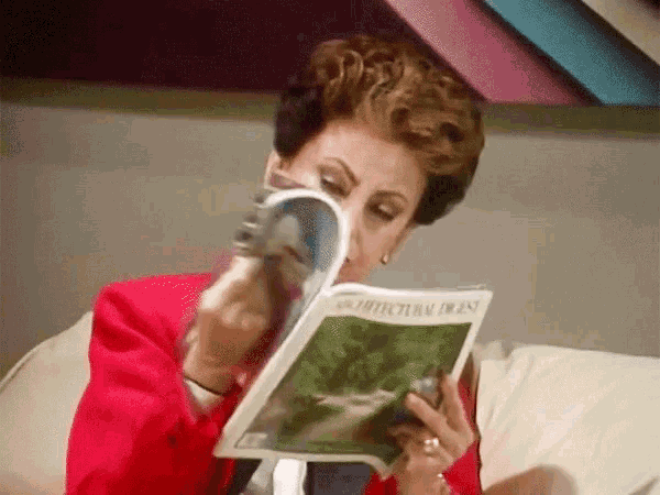 a woman in a red jacket is reading an architectural digest