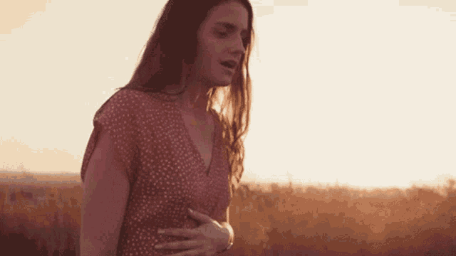 a woman in a red dress is standing in a field with her hands on her stomach .