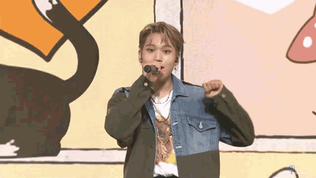 a man in a denim jacket is singing into a microphone in front of a cartoon background