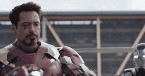 robert downey jr. is wearing a red iron man suit and standing next to another iron man suit .