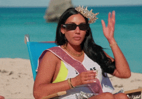 a woman wearing sunglasses and a tiara is sitting on the beach