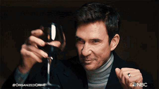 a man is holding a glass of wine with a nbc logo in the background