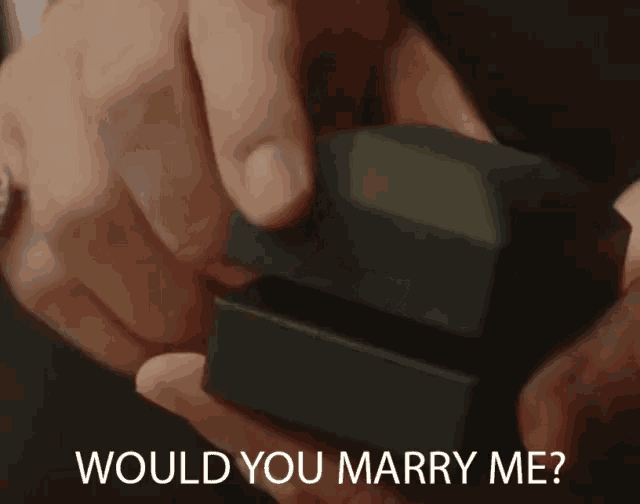 a man is holding a box with a ring in it and the words " would you marry me " above it