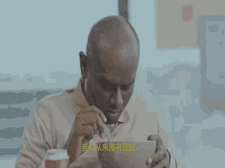 a man is sitting at a table eating a bowl of cereal with a spoon .