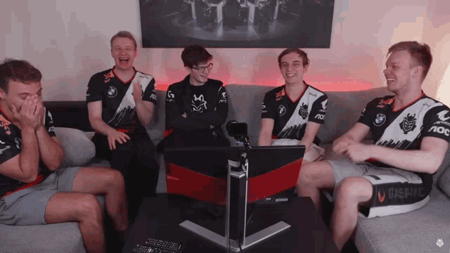 a group of men are sitting on a couch laughing and one of their shirts says aoc on it