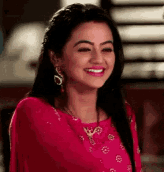 a woman in a pink dress is smiling and wearing earrings and a necklace .