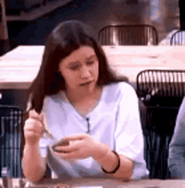 a woman is sitting at a table in a restaurant eating food with a fork .