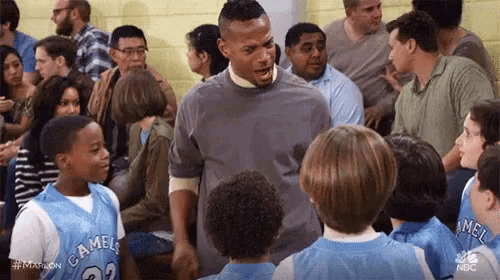 a man is standing in a crowd of people talking to a group of basketball players .