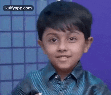 a young boy in a blue shirt is smiling and waving his hand .