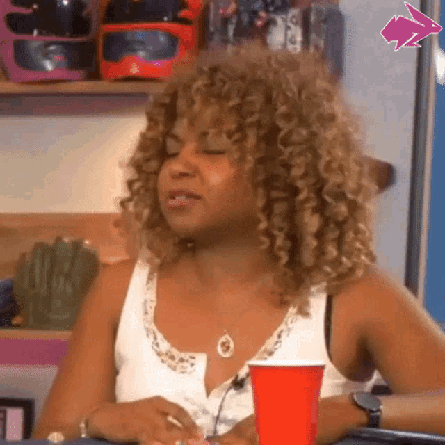 a woman with curly hair is sitting at a table with a red cup and a microphone .