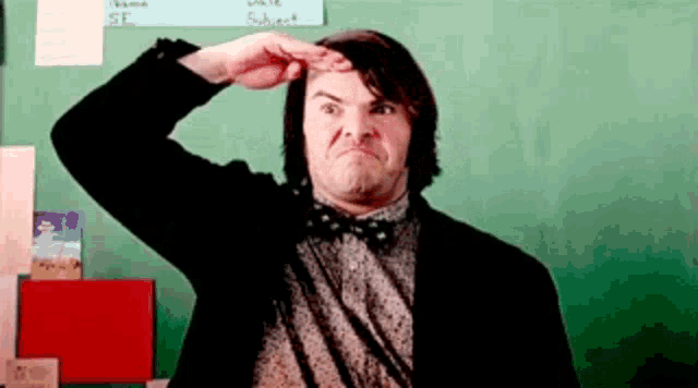a man in a bow tie is saluting in front of a green chalkboard .