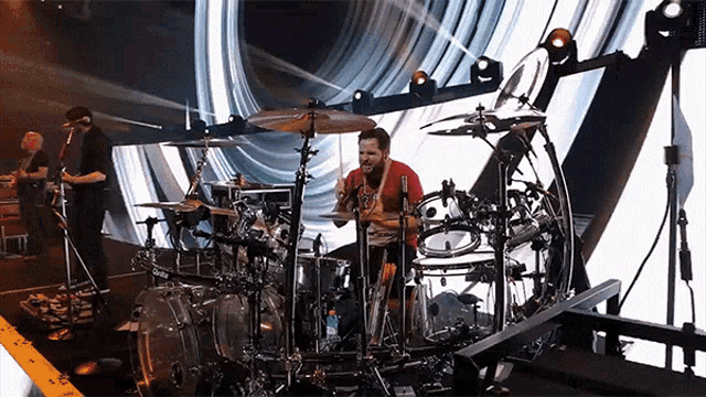 a man in a red shirt is playing the drums on stage