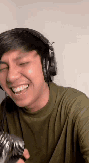 a man wearing headphones and a green shirt is smiling and holding a microphone