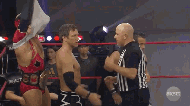 two wrestlers are standing in a ring with a referee in front of them and the referee is wearing an axs uniform