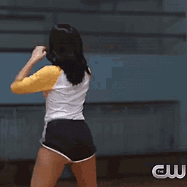 a woman in a yellow and white shirt and black shorts is dancing in front of a cw logo