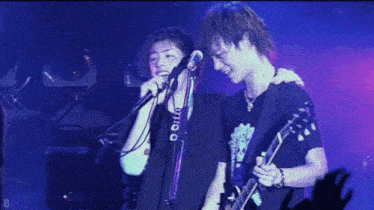 a man is singing into a microphone while another man is playing a guitar on stage .