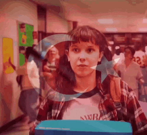 a girl in a plaid shirt is walking down a hallway holding a box .