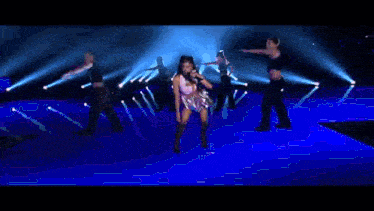 a woman is singing into a microphone on a stage with a group of dancers .