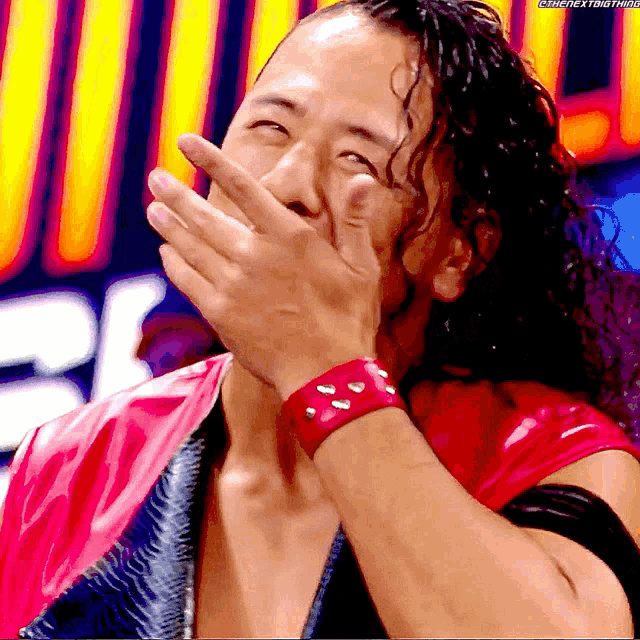 a man with curly hair is covering his mouth with his hand while wearing a red wristband