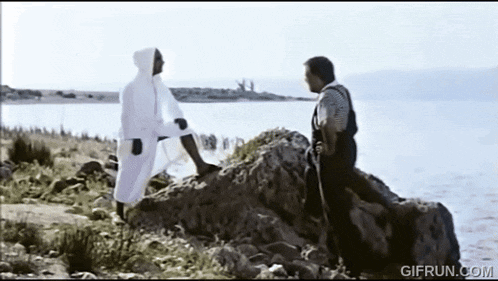 a man in a white robe is standing on a rock near a body of water