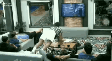 a group of people are sitting on a couch in a living room watching a television .