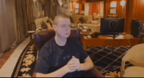 a man is sitting in a chair in a living room with his hands folded in front of him .