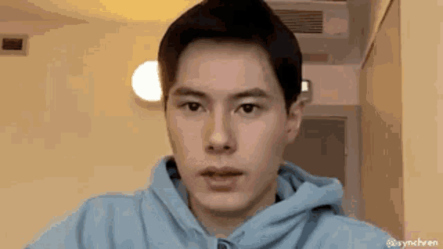 a young man is wearing a blue hoodie and looking at the camera .