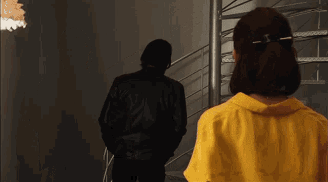 a man in a black jacket and a woman in a yellow shirt are walking down stairs