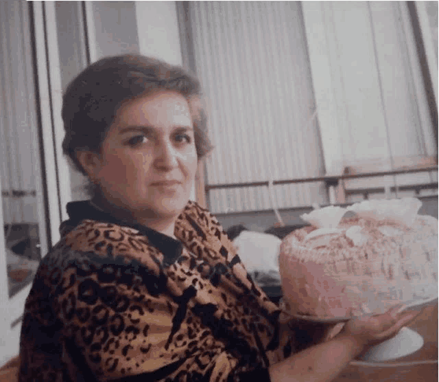 a woman in a leopard print top is holding a pink cake