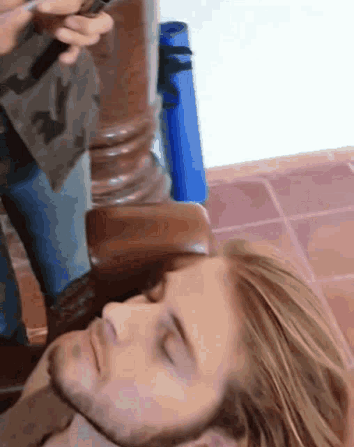 a man with a beard is laying down with his eyes closed and a person standing behind him